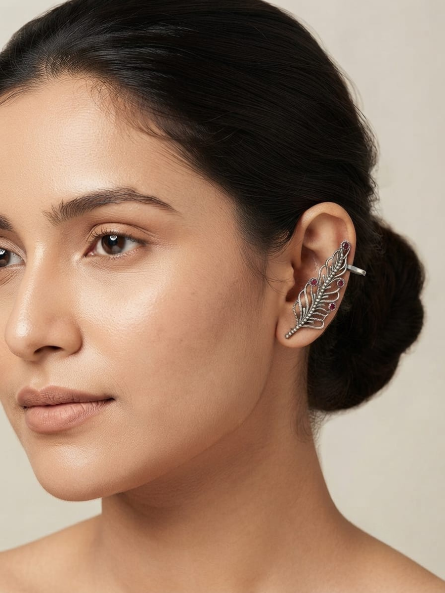 A close-up of a woman's ear wearing a silver-toned feather-shaped ear cuff with small pink gemstone accents