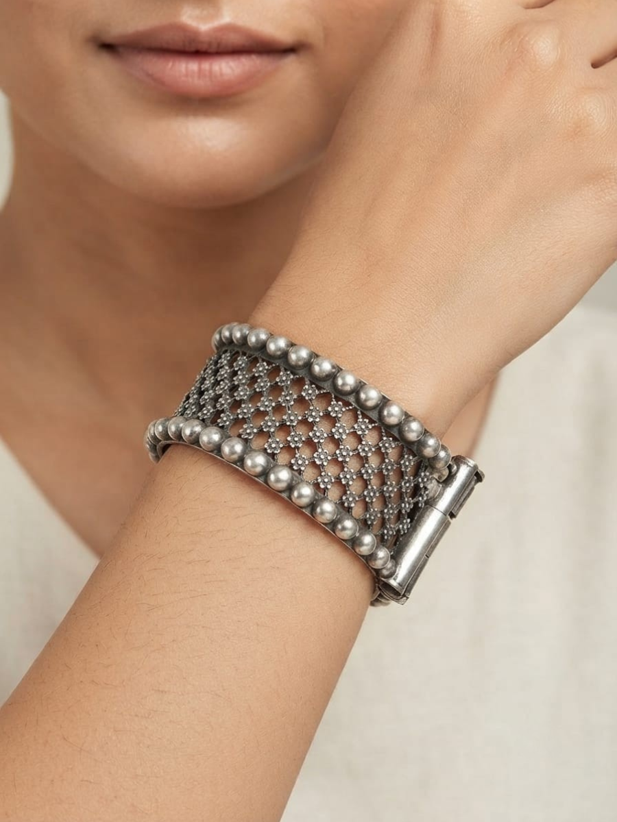 A model is wearing a wide silver mesh cuff bracelet with beaded edges and a clasp closure.