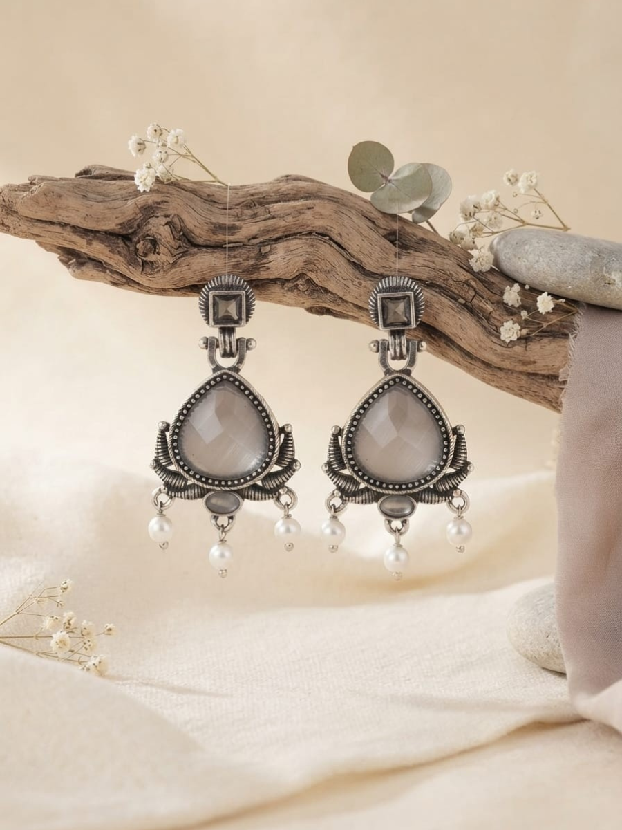 A pair of ornate silver-toned dangle earrings with teardrop-shaped pale gray stone centers and small pearl-like drops