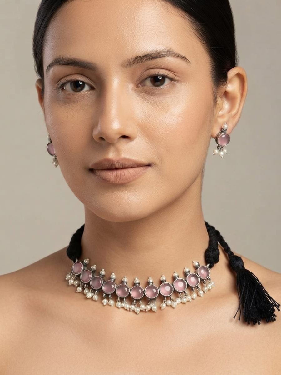 A close-up of a woman wearing a pink and silver beaded choker necklace with matching drop earrings