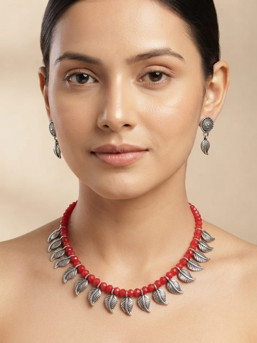 A woman wearing a red beaded necklace with silver leaf-shaped metal accents and matching dangling earrings