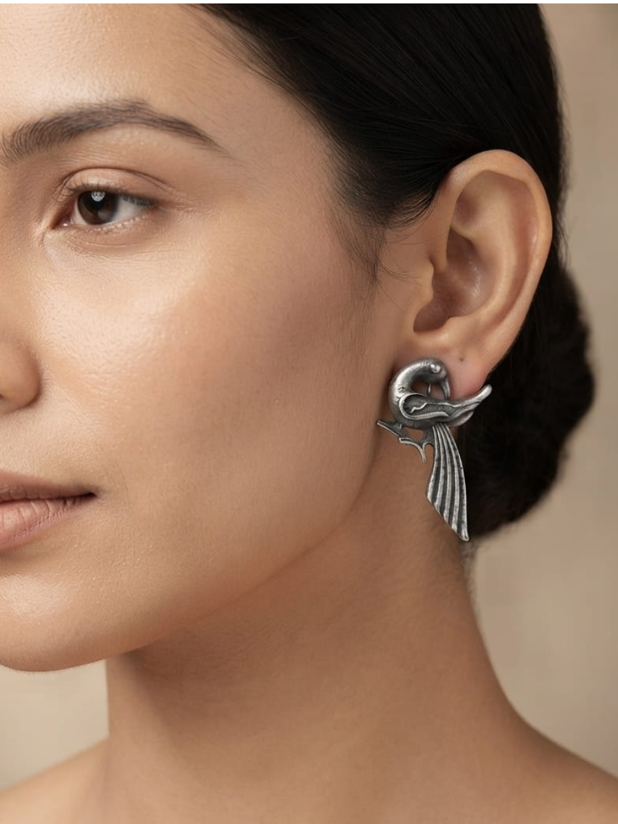 A close-up of a model's ear wearing a textured silver bird stud earring