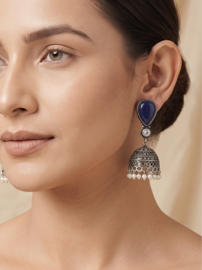 Close-up of ethnic silver-toned jhumka earrings with deep blue gemstones and white bead accents.