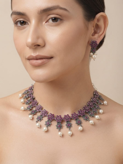 A close-up of a woman wearing a ruby red and silver floral necklace with dangling white pearls, matching drop earrings