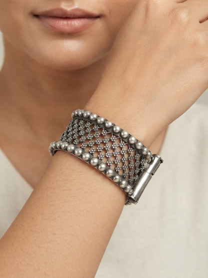 A model is wearing a wide silver mesh cuff bracelet with beaded edges and a clasp closure.