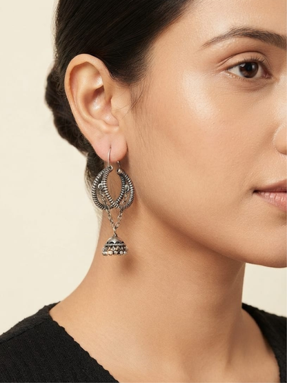 A close-up of a woman wearing a pair of silver-toned, multi-tiered hoop and dangling jhumka earrings