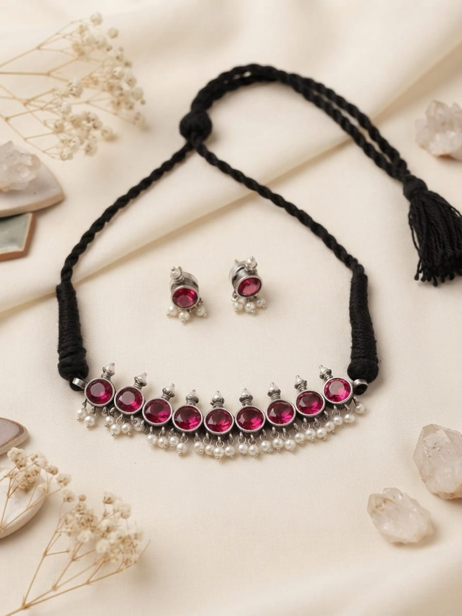 A silver-toned jewelry set featuring a necklace and matching earrings with vibrant pink gemstones and small white pearls