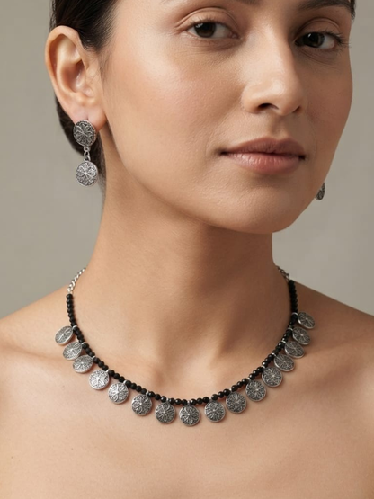 A close-up of a woman wearing a silver coin-style necklace and matching drop earrings