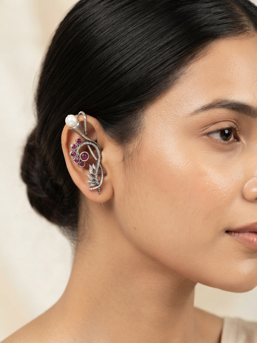 A close-up of a woman's ear wearing a silver-toned ear cuff adorned with a white pearl, pink gemstones, and a small leaf motif.