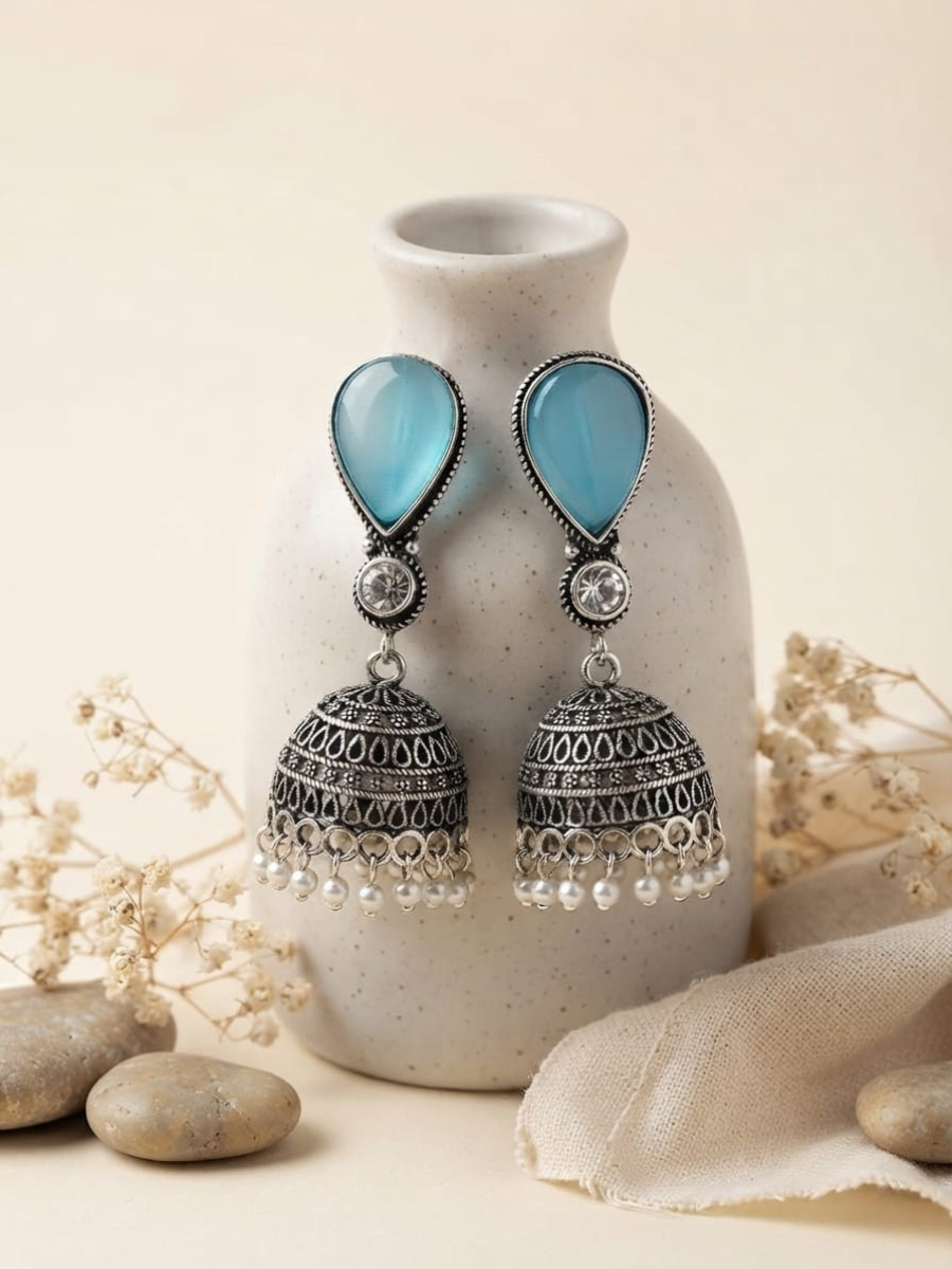 A pair of silver-toned jhumka earrings with light blue teardrop-shaped stones and dangling pearls