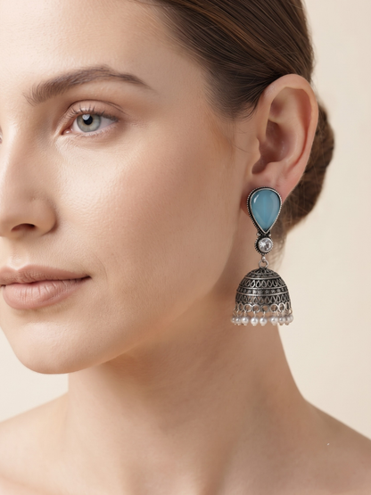 A close-up of a woman wearing a traditional Indian jhumka earring with a light blue teardrop-shaped stone and a jhumka