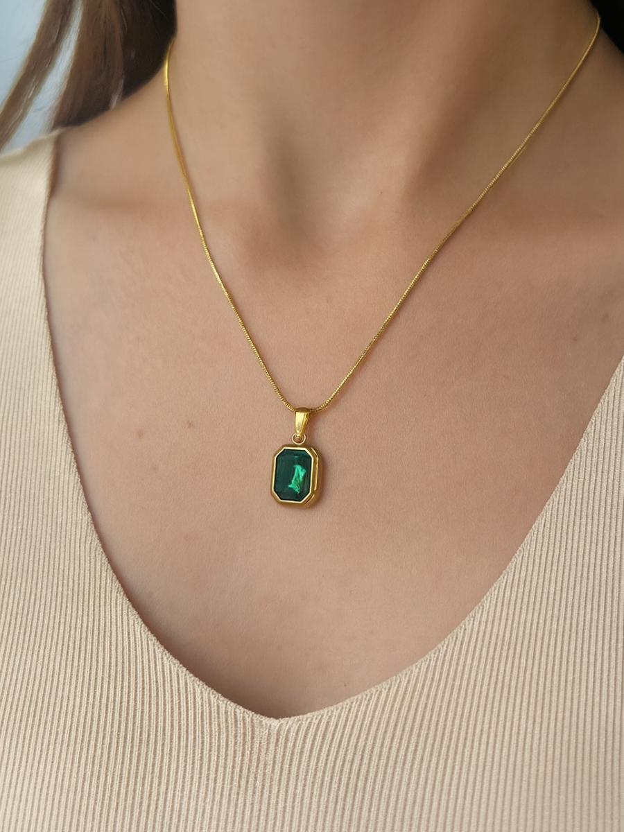 Gold necklace with a green pendant on a person wearing a beige top.