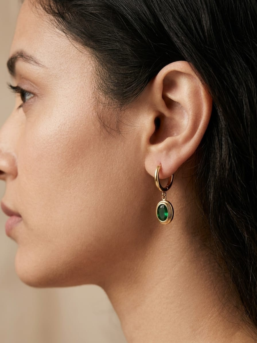 A model is wearing our Trendy Green Stone Oval Drop Golden Huggie Hoop Earrings