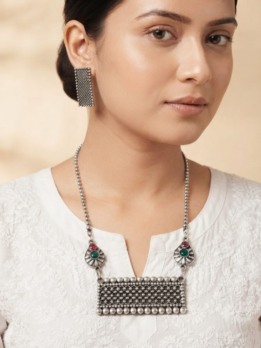 A woman wearing a silver-toned statement necklace with a rectangular beaded pendant and matching rectangular earring
