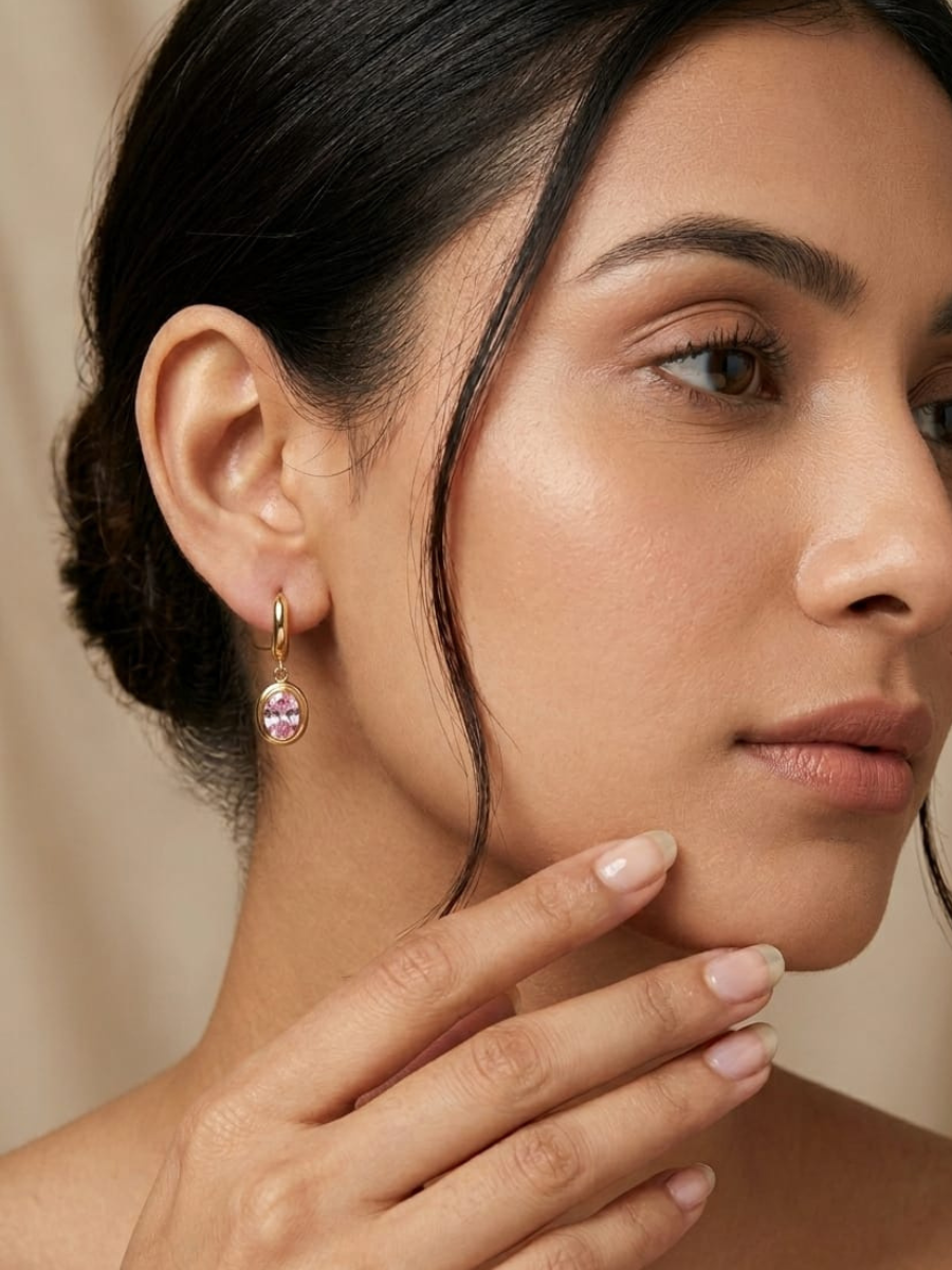 A model is wearing our Trendy Pink Stone Oval Drop Golden Huggie Hoop Earrings